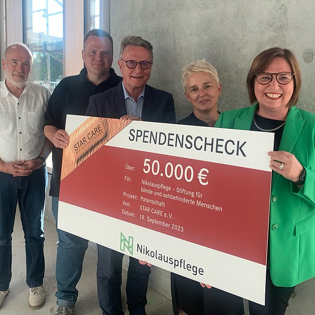 Drei Männer und zwei Frauen halten einen Scheck in die Höhe