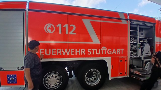 Ein Feuerwehrauto steht vor dem Schulgebäude. Ein Schüler berührt das Auto mit seiner Hand