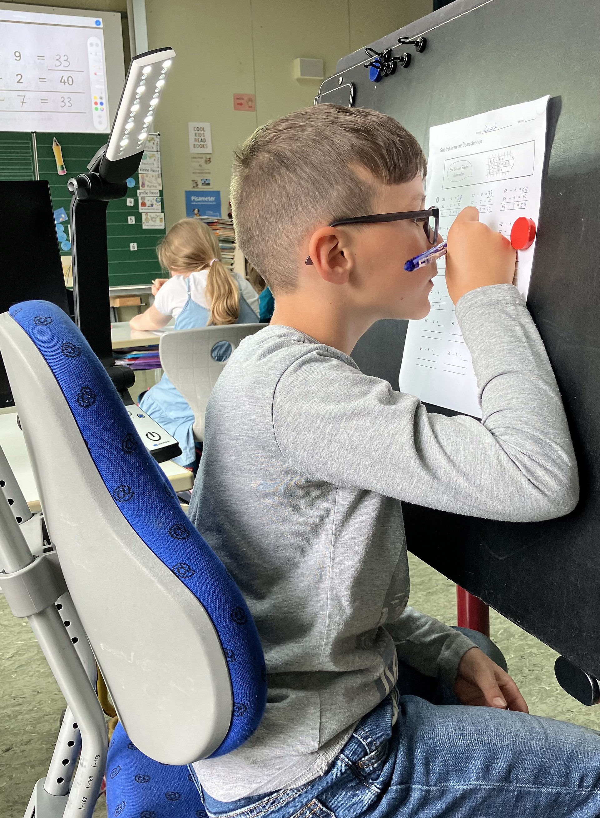 Ein Schüler sitzt ganz nah an einer Tafel und schreibt etwas auf ein Blatt papier