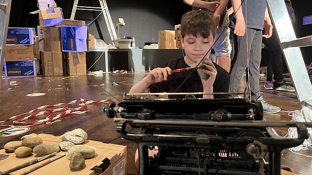 Ein Schüler sitzt auf der Bühne hinter der einer alten Schreibmaschine