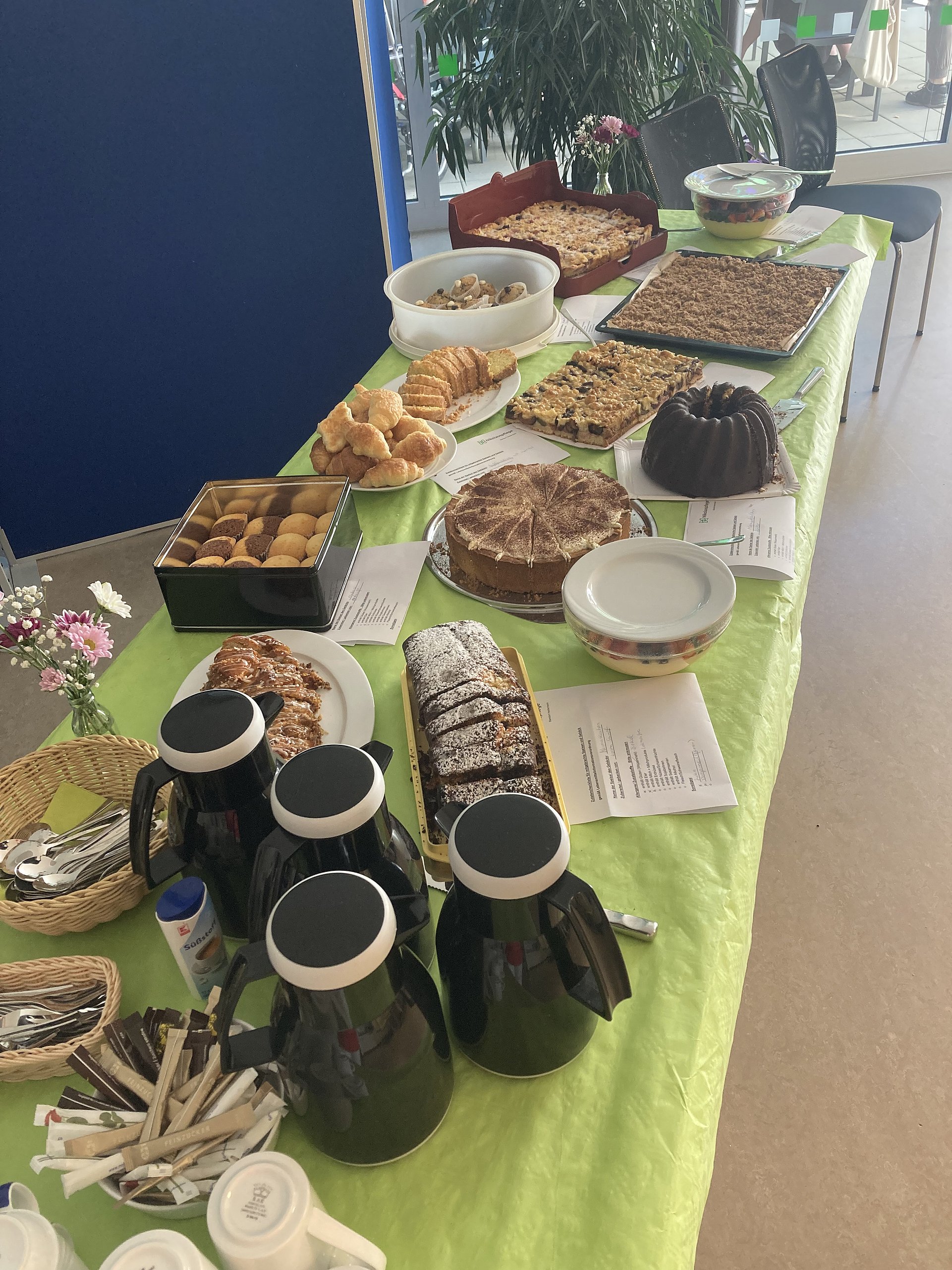 Buffet-Tisch mit Kuchen und Gebäck auf einer hellgrünen Tischdecke.