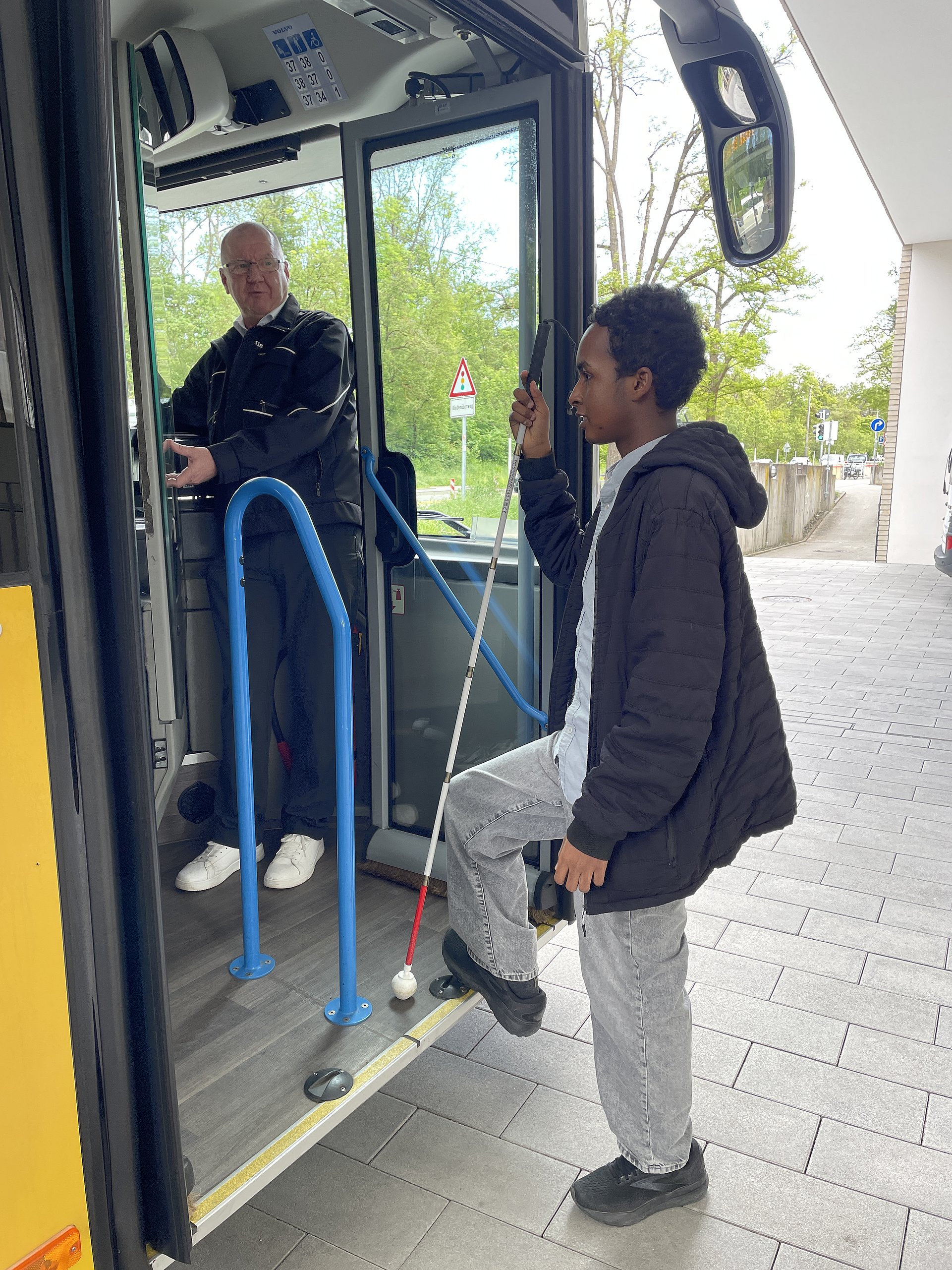 Ein Schüler mit einem Langstock steigt in einen Bus rein