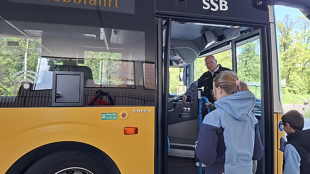 Schülerinnen und Schüler steigen in einen Bus ein. Der Busfahrer steht neben der offenen Tür