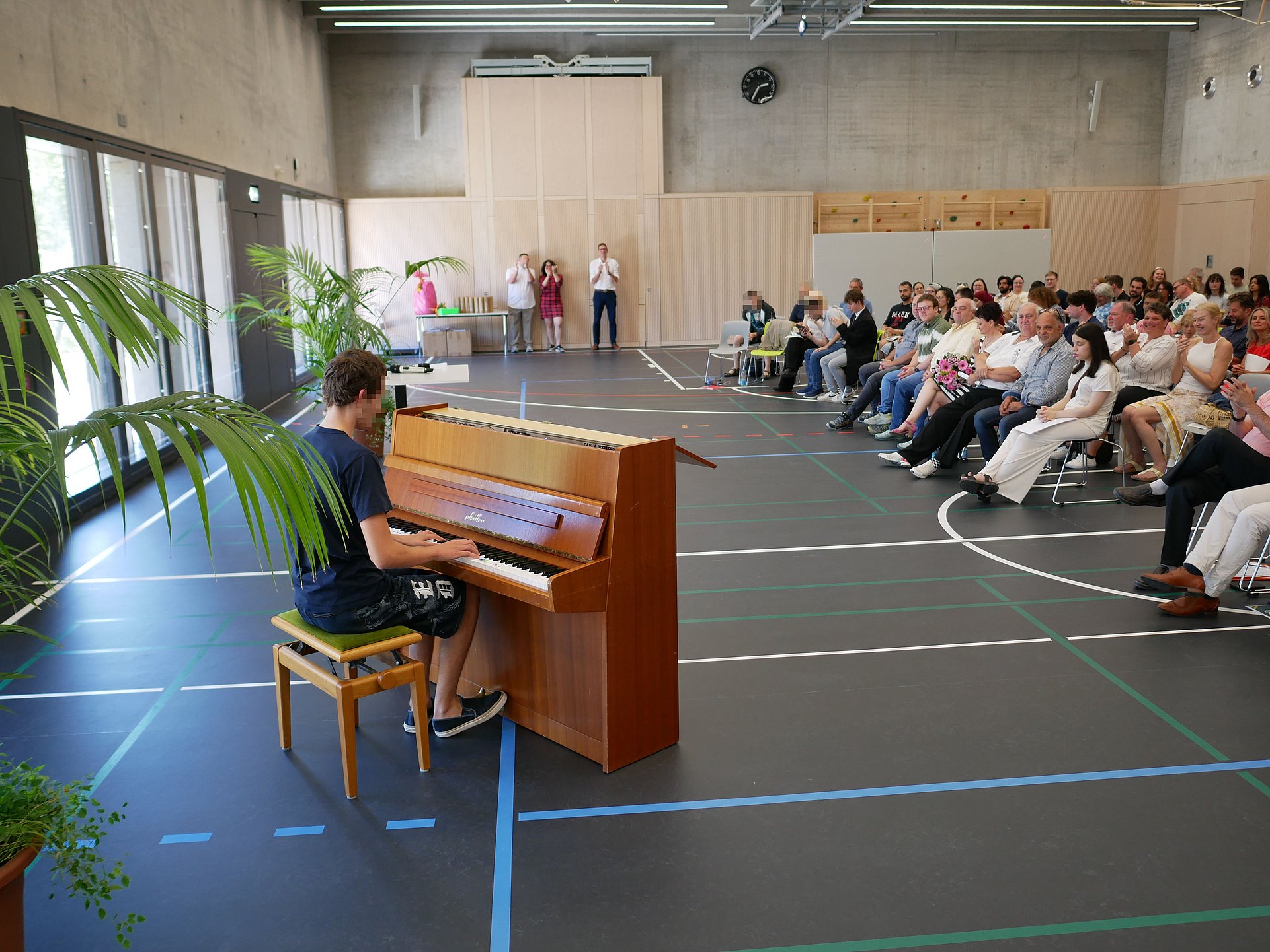 Ein junger Mann spielt an einem Klavier in der Turnhalle der Schule. Vor ihm sitzt das Publikum und hört zu