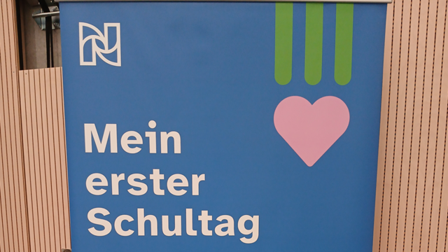 Auf einem blauen Plakat steht in weißer Schrift Mein erster Schultag. Daneben ist ein Rosa Herz. Darüber das weiße Logo der Nikolauspflege