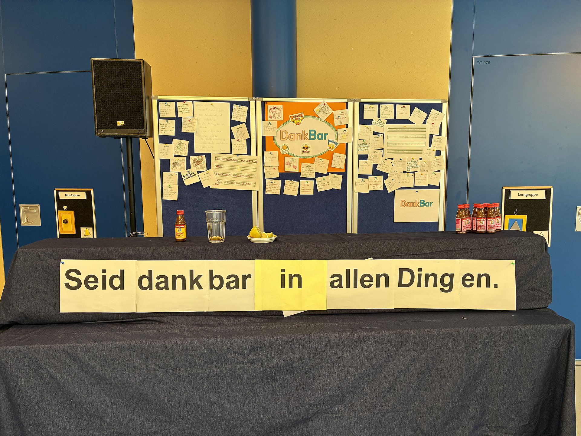 Auf einem Kirchaltar stehen Pinwände, an denen viele beschriftete Zettel angebracht sind. Unten auf dem Altar hängt ein großes Banner auf dem steht: Seid dankbar in allen Dingen. Links auf dem Altar steht ein Lautsprecher