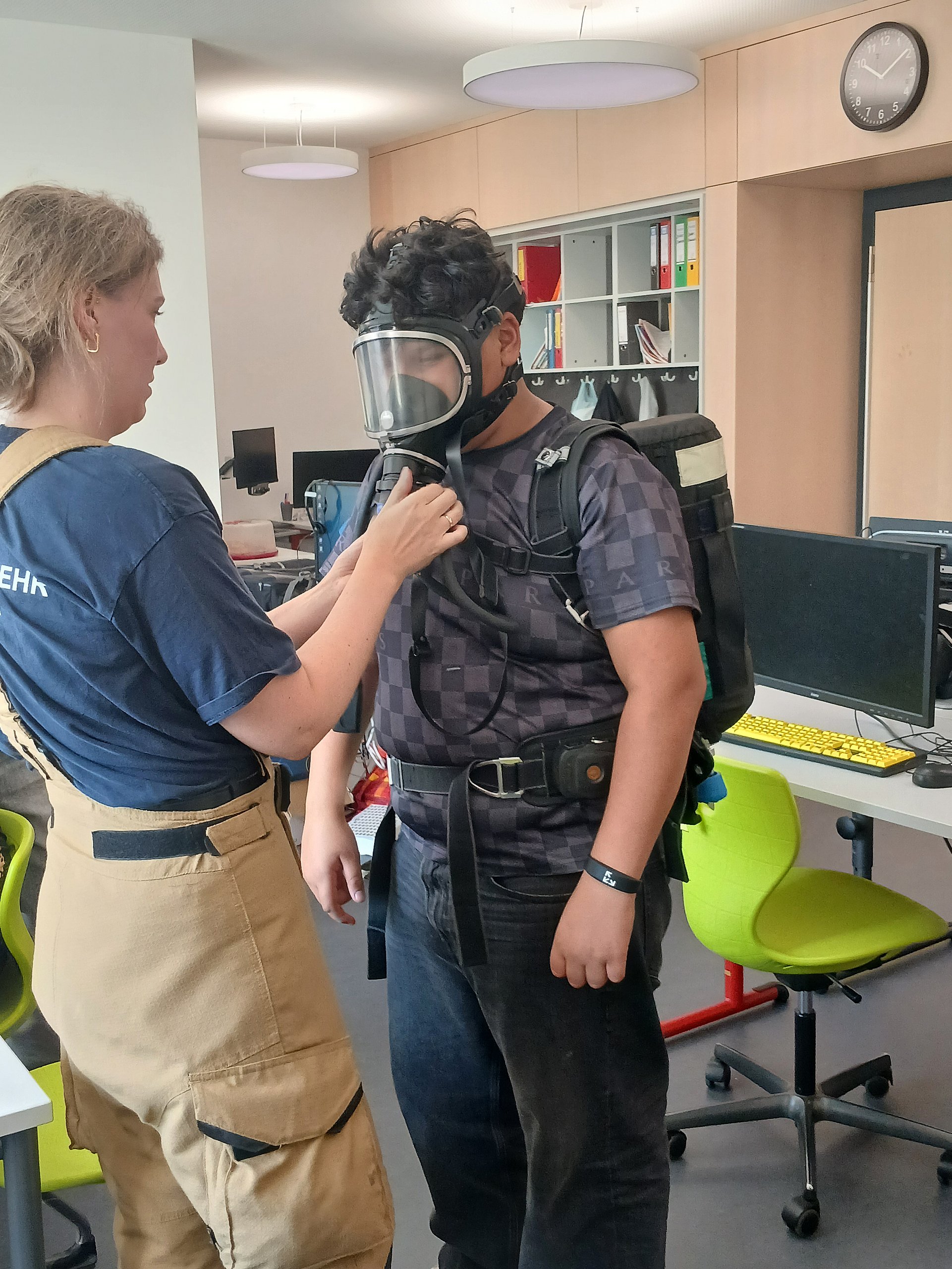 Eine Feuerwehrfrau justiert bei einem Schüler eine Gasmaske